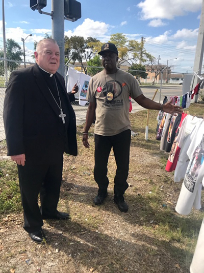 Archbishop Thomas Wenski on March 24 visited the site of Operation Hunger Strike, a protest against gun violence in urban communities staged by nine men affiliated with a group called The Circle of Brotherhood. Here he stands next to the clothesline hung with T-shirts bearing the faces of people killed by gun violence.