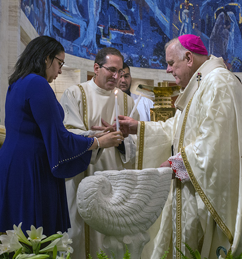 Archbishop Thomas Wenski hands catechumen Nathalie Matos a candle symbolizing her moving from death to life in Christ through baptism.