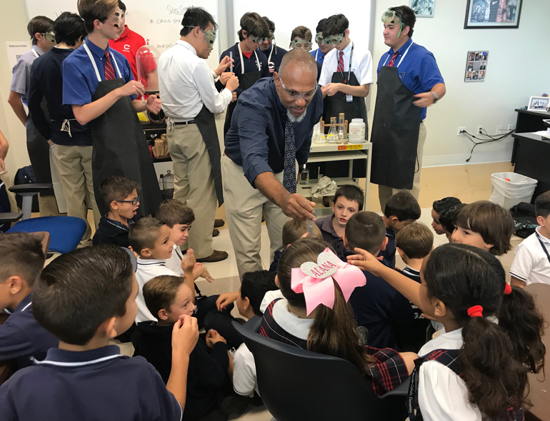 Take a closer look: Columbus High AP Chemistry teacher Ludwig Baez shows first graders from St. Brendan School a test tube used in lab experiments. The young students came to visit the high school next door during a STREAM Day field trip.