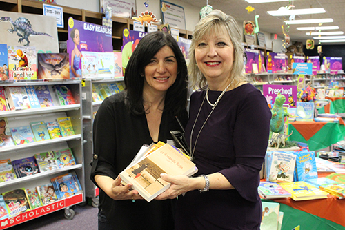 Author Christina Diaz Gonzalez, left, presents copies of all her books to St. Mark School Media Specialist Sandy Garcia, who will prepare them for circulation in the school's library. Diaz Gonzalez was invited to St. Mark March 25 to kick off the school's book fair and discuss her books with students.