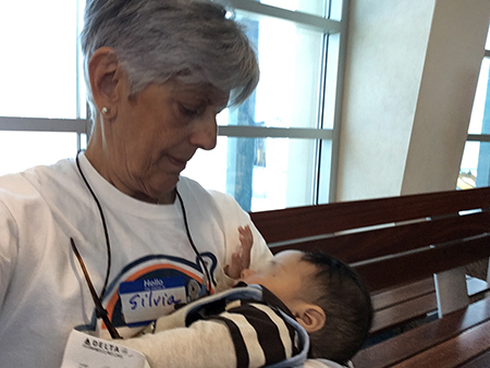 Silvia Muñoz, director of social action for the Jesuits’ Pedro Arrupe Institute in Miami, holds a child while the mother shows her papers to TSA officials. During her two weeks as a volunteer at an El Paso, Texas, shelter, Muñoz would accompany immigrants to the airport once they obtained the airfare to reunite with family members or sponsors in the U.S.