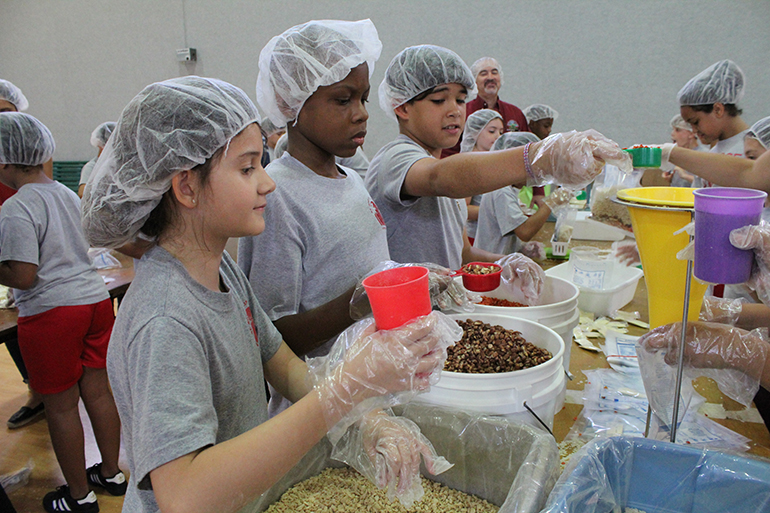 Los estudiantes de cuarto grado de la escuela St. Rose of Lima esperan su turno para poner porciones de verduras, frijoles pintos y soja en polvo, durante el evento de empaque de comidas, Meals of Hope, en el gimnasio de la escuela, el 30 de abril.