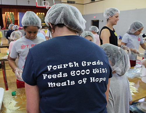 Encuadre de la camiseta de la maestra de cuarto grado de la escuela St. Rose of Lima, Paulina Cuadrado, anunciando el evento de empaque de comidas, Meals of Hope.