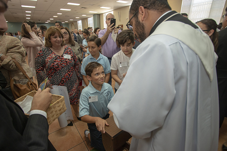 El recién ordenado P. José Enrique López bendice a un estudiante de quinto grado de la escuela St. Bonaventure, en Davie. La clase de quinto grado lo "adoptó" el año pasado como parte de sus lecciones sobre los sacramentos que incluye las órdenes consagradas. Esta fue la primera ordenación que vieron los nueve niños que asistieron. "Es increíble", dijo su maestra, Rosie DiLella (en la parte trasera). "Los niños realmente aprenden mucho. En lugar de estudiar los libros, pueden verlo directamente".