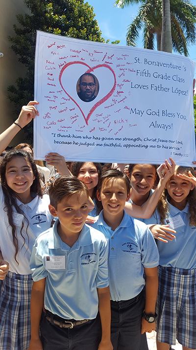 Los estudiantes de quinto grado de la escuela St. Bonaventure sostienen una pancarta que hicieron para su seminarista "adoptado", el P. José Enrique López, después de presenciar su ordenación, el 11 de mayo, en la Catedral St. Mary.