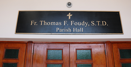 A plaque over the door of the St. Coleman Parish Hall features the name of Father Thomas F. Foudy, who died May 19, hours before the parish gathered to mark its 60th anniversary. The day turned into a celebration of Father Foudy's life. According to those close to him, Father Foudy, former pastor, loved St. Coleman Parish and School and was dedicated to Catholic education, supporting and helping with various initiatives to expand facilities and opportunities for students. The parish and school dedicated the parish hall to him as a permanent tribute.