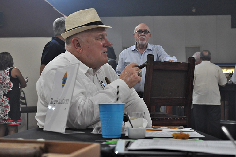 Archbishop Thomas Wenski relaxes with a cigar near the sign-in table for the annual Havana Nights fundraiser for Catholic Charities' Unaccompanied Minors Program.