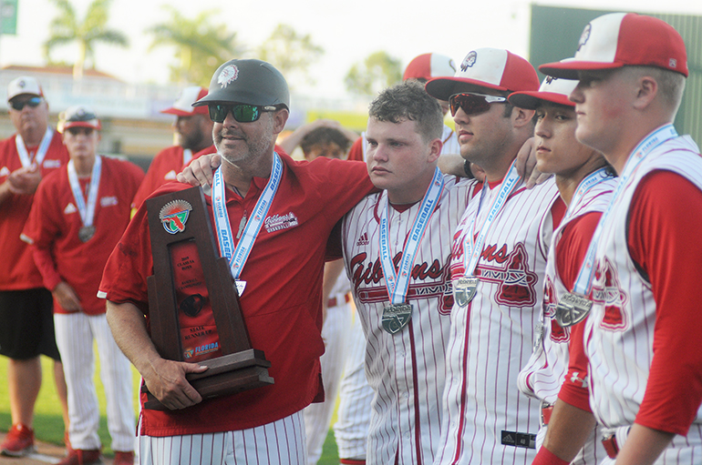 Cardinal Gibbons head coach Jason Hamilton, left, holds the runner-up trophy with seniors Kevin Hirsch, John Diaz, Kyle Kuramoto and Keanu Buerosse following the Chiefs' 6-3 eight-inning loss to Melbourne Central Catholic in the Class 5A baseball state championship game at Hammond Stadium in Fort Myers.