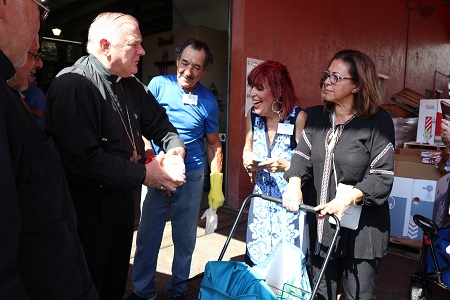 El Arzobispo Thomas Wenski le entrega un pollo entero a María Melián, durante su visita al nuevo local del banco de comida de la Sociedad San Vicente de Paul de la parroquia Mother of Christ, el 8 de junio.