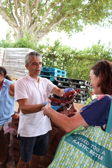 Andrés Avilán, uno de los cerca de 30 voluntarios que ayudan en la distribución de la comida dos veces al mes, entrega alimentos a una beneficiaria del banco de comida de la parroquia Mother of Christ, que recientemente se mudó a un nuevo local en Kendall, al sur del aeropuerto Tamiami.