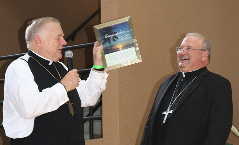 Archbishop Thomas Wenski presents Auxiliary Bishop Peter Baldacchino with a framed version of a congratulatory ad purchased by the Archdiocese of Miami for Agua Viva, the newspaper of the Diocese of Las Cruces, New Mexico. The photo, taken by Sister Elizabeth Worley, a Sister of St. Joseph who serves as archdiocesan chancellor for administration, is a sunset view of the bay close to St. Kieran Church, Miami, where Bishop Baldacchino served as pastor for five years.