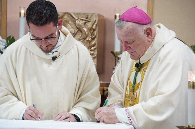 Archbishop Thomas Wenski and Father Bryan Garcia sign the papers officially naming him pastor, rather than administrator, of St. Bernadette Parish in Hollywood, June 15, 2019.