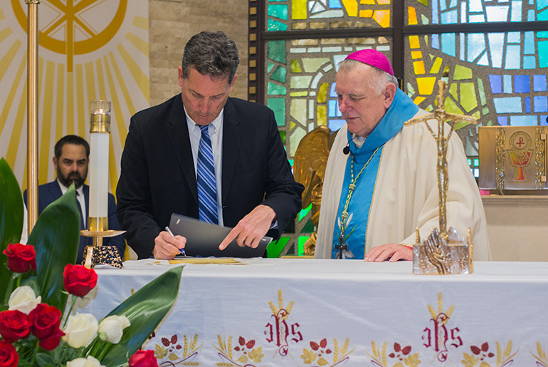 Archbishop Thomas Wenski looks on as Key Biscayne Mayor Michael Davey signs the consecration document for the village.