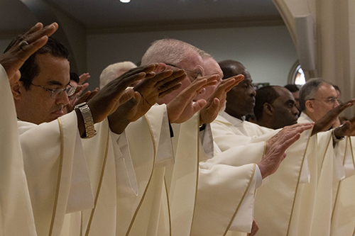Priests extend their hands to join Archbishop Thomas Wenski in blessing the oil of chrism during the annual Mass of chrism, celebrated the Tuesday of Holy Week, April 16, 2019.