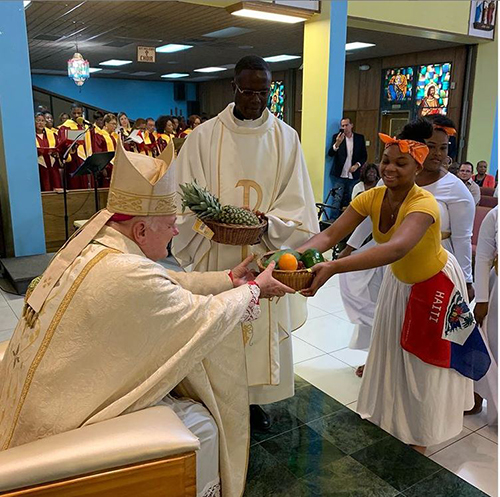 Archbishop Thomas Wenski receives the offertory gifts during Mass at St. Helen Parish in Lauderdale Lakes Aug. 18. He celebrated a special trilingual Mass for the feast day of St. Helen. Looking on is Father Lucien Pierre, St. Helen's pastor.