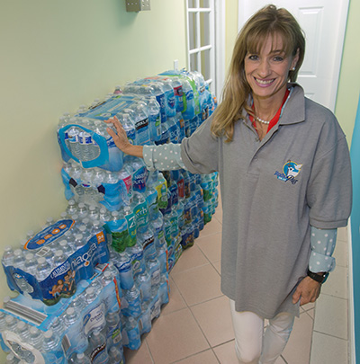 Radio Paz volunteer MariCarmen Oar stands beside some of the bottled water that donors have begun to bring to the studios of Radio Paz for Bahamas relief after Hurricane Dorian ravaged Grand Bahama, Freeport and Abaco.