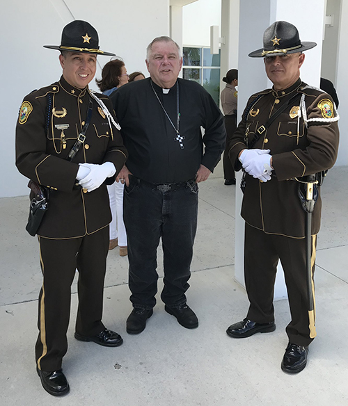 Archbishop Thomas Wenski poses with two Miami-Dade County police officers in dress uniform after the conclusion of the Blue Mass he celebrated for fire, police and emergency personnel at Our Lady of Guadalupe Church in Doral, Sept. 27, 2019. The photo was posted on the archbishop's Twitter feed @ThomasWenski.