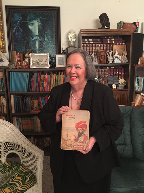 Carlota Morales is shown here amid the memorabilia of 50 years in education at her Shenandoah home, where she has lived since 1967. She is holding the algebra textbook she brought with her when she left Cuba in 1961.