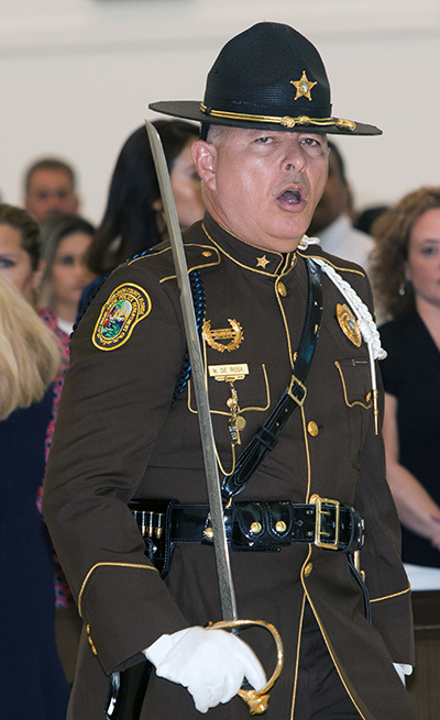 Miami Dade Police Officer Marcos DeRosa, an honor guard member, calls out orders to fellow officers carrying the flags of their various police departments as they process into Our Lady of Guadalupe Church for the Blue Mass.