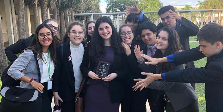 Immaculata-La Salle's Debate Team pose for a photo pointing out senior Isabella Perez's sixth place win in the Lincoln-Douglas debate of the Oct. 12 competition at West Broward High School.
