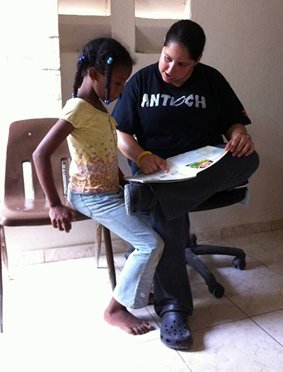La misionera de Amor en Acción, Jeannette Victoria, lee con una nueva amiga de la República Dominicana, durante un viaje misionero.