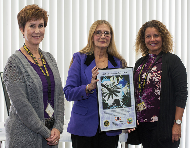 Karen Brent, left, and Edyleidy Mirabel-Urra, from the Miami Gardens Police Victims Advocate Service, pose with Susan Buzzi, center, who is holding one of her photos on domestic violence.