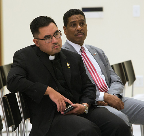 Father Philip Tran, Catholic Campus Ministry chaplain at the University of Miami, and Patrick Stewart, UM's executive director of Development, College of Arts and Sciences, listen to Archbishop Thomas Wenski speak at the UM forum on "Who Is Our Neighbor? Immigration in Light of Catholic Social Teaching," held in the Newman Alumni Center, Oct. 21, 2019.