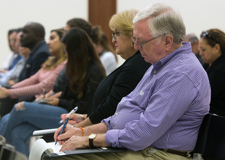 Peter England and Julie Romero, of St. Louis Church in Pinecrest, take notes during Archbishop Thomas Wenski's talk at a University of Miami forum on "Who Is Our Neighbor? Immigration in Light of Catholic Social Teaching," held in the Newman Alumni Center, Oct. 21, 2019.