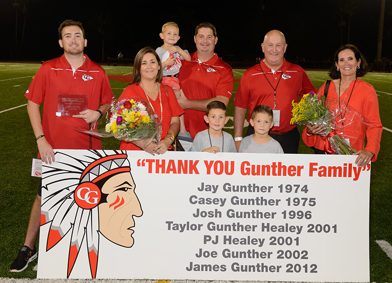 The Gunther family poses together with their commemorative plaque following the halftime recognition ceremony. Back row, from left: James Gunther, PJ Healey, Reece Healey (child being held), Jay Gunther, Terry Gunther. Front row, from left: Taylor Gunther Healey, Peyton Healey, Graeme Healey.