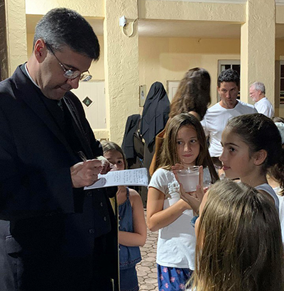 Father Manny Alvarez, pastor of Little Flower Church, Coral Gables, answers some questions from St. Theresa School's student-reporters after the dedication of the new Alumni Plaza.