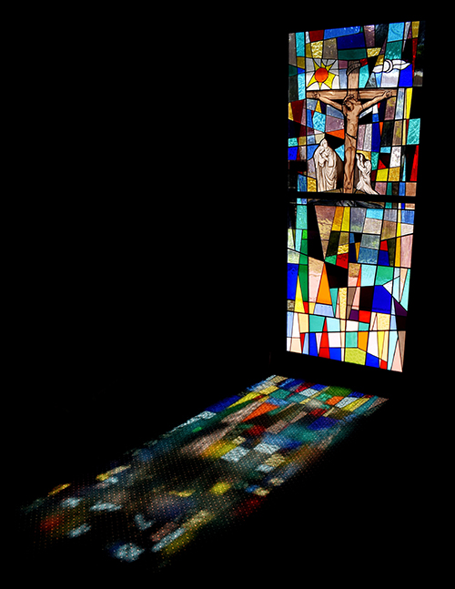 A crucifixion window casts a multicolored shadow at St. Ambrose Church. The window is part of the church's Pietá Chapel, for private devotions.