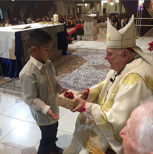 Archbishop Thomas Wenski receives a gift from a child during the last Mass of the traditional Filipino novena of Simbang Gabi, which he celebrated Dec. 23, 2019, at St. David Church in Davie. "After Mass (with a full church), a delicious meal of Filipino food was served to all," the archbishop wrote on his Instagram account.