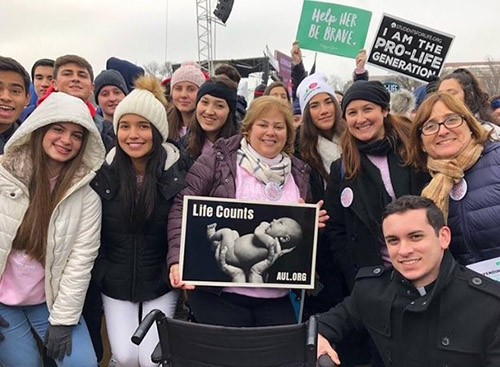 Father Michael Garcia, archdiocesan chaplain for the high school contingent to the 2019 March for Life, bottom right, poses with a group of students from Our Lady of Lourdes Academy and St. Brendan High School in Miami, along with Lourdes chaperones Martica Castellanos, center, and Maria Romero, second from right, as well as St. Brendan chaperone Rosa Mari Alvarez, far right.