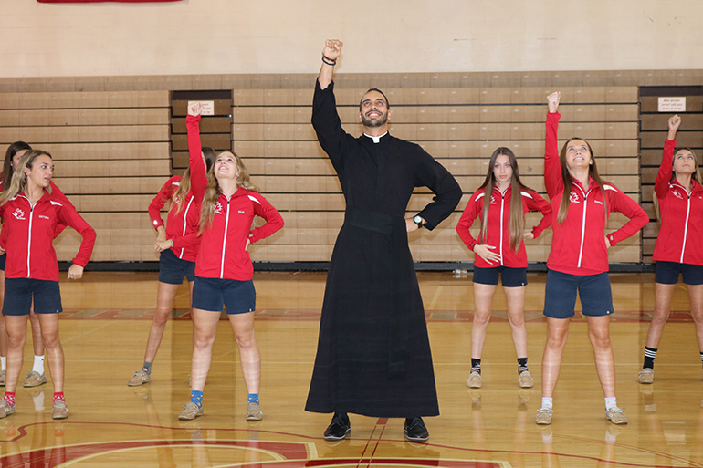 El P. Ricardo Rivera efectúa algunos movimientos de baile con el equipo de danza de la escuela Cardinal Gibbons.