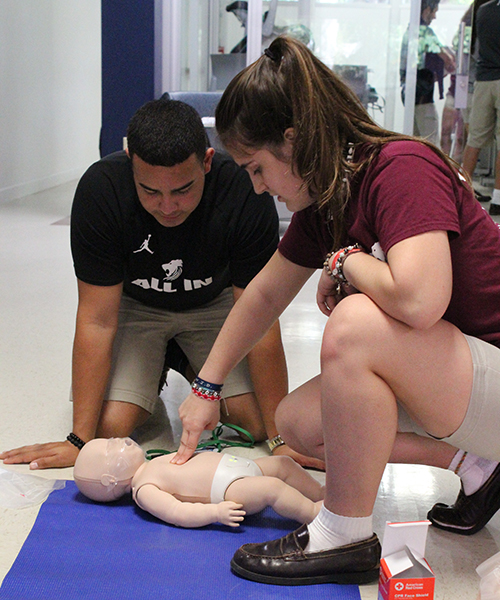 First aid even on the smallest: Immaculata-La Salle High students practice CPR compressions on an infant dummy at a makeshift first aid Health Science station at the STEAM Day celebration exhibit last November.