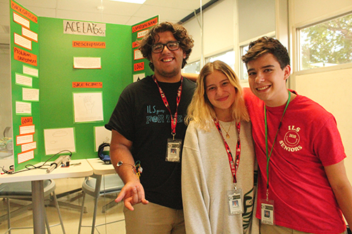 Los creadores de ACE LABs en la escuela secundaria de Immaculata-La Salle, Ernesto Walter, Annabella Iurman y Christopher Solanilla, se retratan frente a su proyecto durante la celebración del Día Nacional de STEAM. El trío creó un dispositivo sensorial muscular para las personas que sufren lesiones del plexo braquial. El dispositivo los ayuda a levantar y bajar el brazo, así como a levantar pesos.