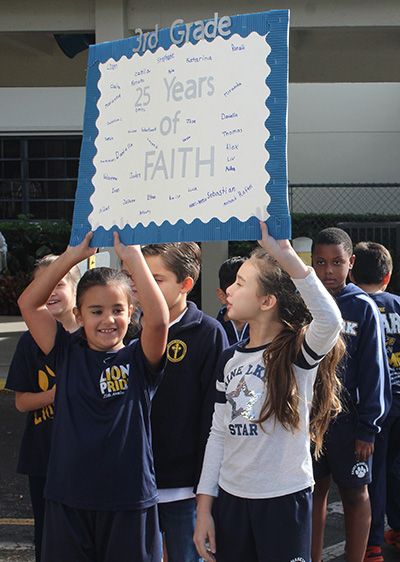 Two St. Mark School third graders hold up a poster signed by all of their classmates, celebrating the school's 25th anniversary. On Jan. 24, 2020, students celebrated their school and also kicked off Catholic Schools Week with the first pep rally in the school's history.