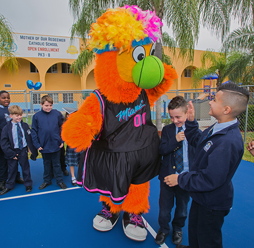 Fourth-graders Matthew Camert and Kevin Martinez high-five the Miami Heat's Burnie after the blessing of Mother of Our Redeemer's new basketball-volleyball court, Jan. 27, 2020.