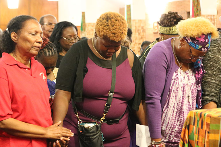 Faithful gather in prayer around the altar during Revival 2020's opening night, Feb. 16 at Holy Redeemer Church in Miami. Anita Victor is shown in the center wearing a purple dress. This was the first time she had participated in the annual event and appeared moved as she prayed.