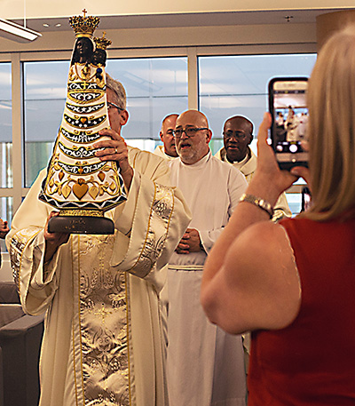 El diácono Ernesto Sosa lleva la imagen de Nuestra Señora de Loreto para iniciar la misa, el 17 de febrero de 2020, en el Aeropuerto Internacional de Miami, mientras los asistentes toman fotos. La estatua fue traída por el capellán del aeropuerto de Madrid, el P. Urbano Monedero, como parte de una peregrinación jubilar en todo el mundo. Nuestra Señora de Loreto es la patrona de las personas involucradas en la aviación, así como los constructores y trabajadores de la construcción.