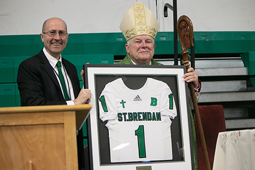Archbishop Thomas Wenski holds up the St. Brendan #1 jersey he received from the high school's principal, left, Jose Rodelgo Bueno. The archbishop celebrated Mass with St. Brendan High School students and staff before blessing the Miami school's new athletic fields, Feb. 19, 2020.