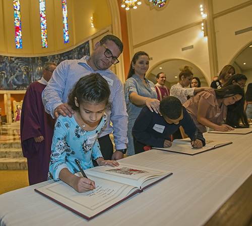 Catechumen Aislinn Izquierdo signs the Book of the Elect as her sponsor, Christopher Munoz, looks on. She was among about 550 catechumens who took part in one of the two Rite of Election ceremonies held March 1, 2020, at St. Mary Cathedral.