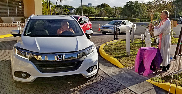 Father Bob Tywoniak blesses cars with a monstrance during a drive-through blessing at Blessed Sacrament Church in Oakland Park March 22, 2020.