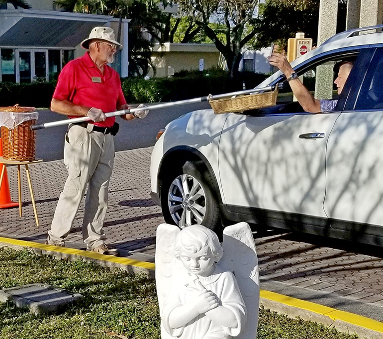 A parishioner holds out a basket on a pole to collect offerings during a drive-through blessing at Blessed Sacrament Church in Oakland Park March 22, 2020.