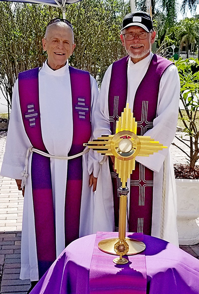 Father Bob Tywoniak, right, shows the monstrance he used in a recent drive-through blessing at Blessed Sacrament Church, Oakland Park. Next to him is Father Dennis Rausch, who assists at the church.