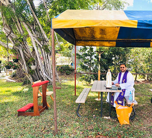 In late March, Father Julio De Jesus, pastor of St. Benedict in Hialeah, poses in front of the outdoor confessional space he improvised on the parish grounds. Note the social distance.