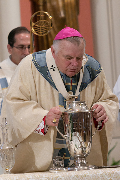 Archbishop Thomas Wenski blows into the oil of chrism,  consecrating it for use in ordinations of bishops and priests and consecrations of churches and altars.