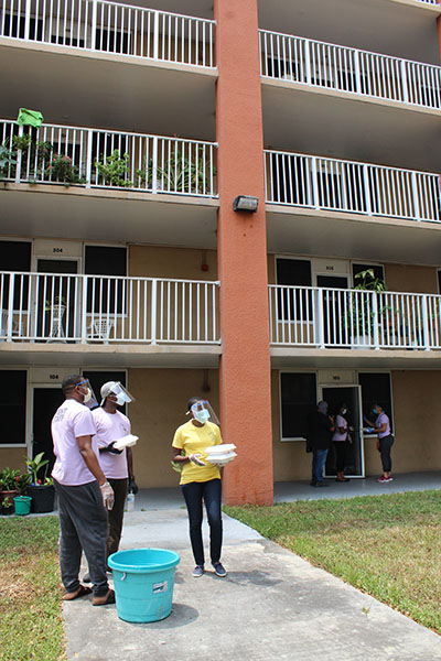 Volunteers from Notre Dame d'Haiti Mission visit an apartment complex and call for residents to come down and receive hot meals. The meals were cooked and delivered on April 11, 2020.
