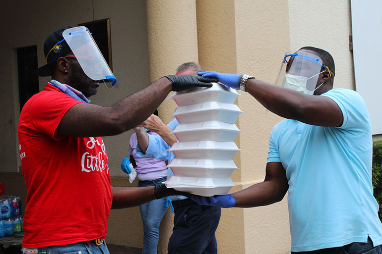 Volunteers from Notre Dame d'Haiti Mission start a human chain, passing hot meals from one to another, until the truck that will deliver the meals is filled to capacity. They then headed out to the Little Haiti neighborhoods to distribute meals to the many elderly residents who are precautionarily homebound because of COVID-19.
