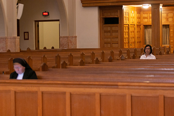 Two staff members, seated rows apart, are the only ones present at Miami's St. Mary Cathedral as Archbishop Thomas Wenski celebrated Palm Sunday Mass in the midst of the coronavirus pandemic, April 5, 2020. How will parishes maintain social distancing once Masses with a congregation resume, given the fact that a coronavirus vaccine is months away from development and widespread distribution?